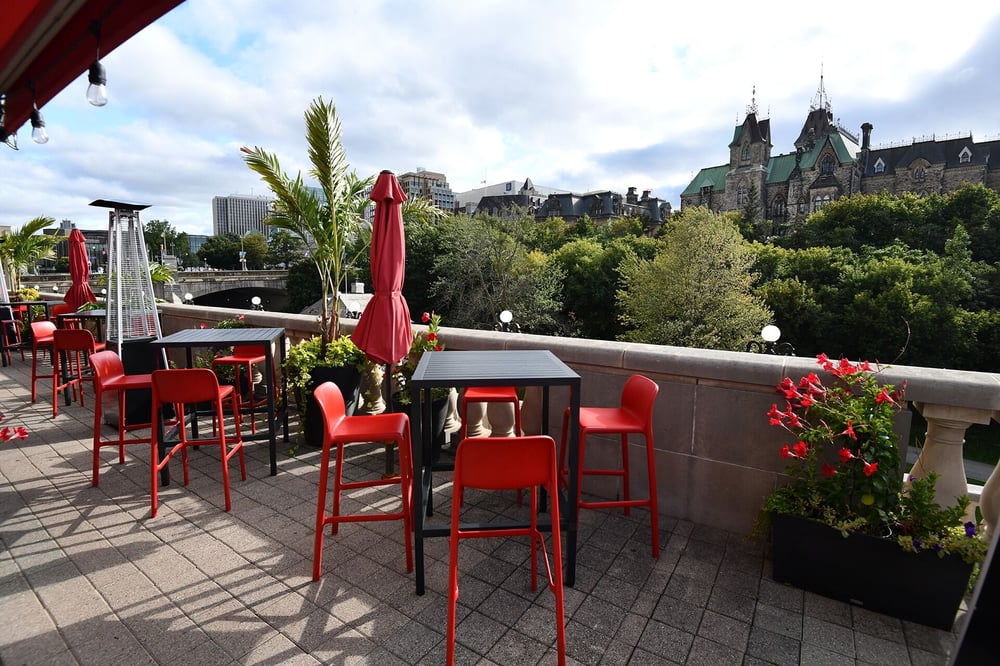 Outdoor seating area with black high top tables, red bar stool seats overlooking a chateau building